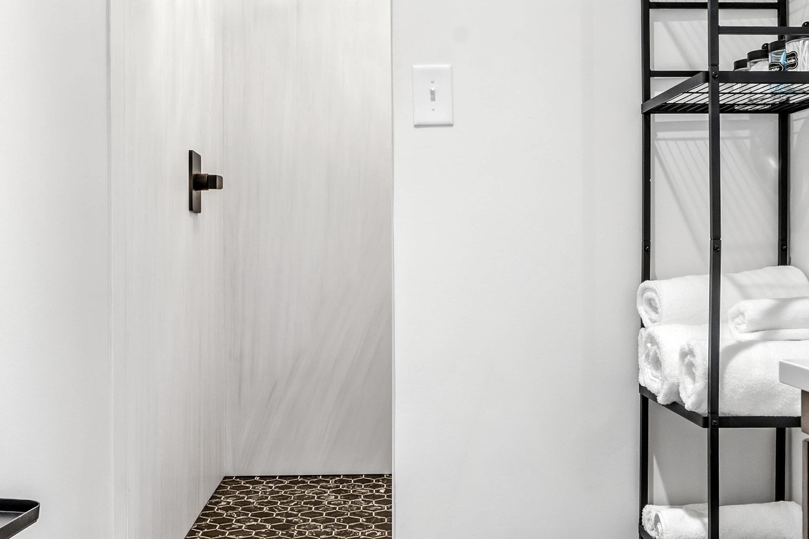 A bathroom with a white door, a black towel rack with towels, and a patterned floor.