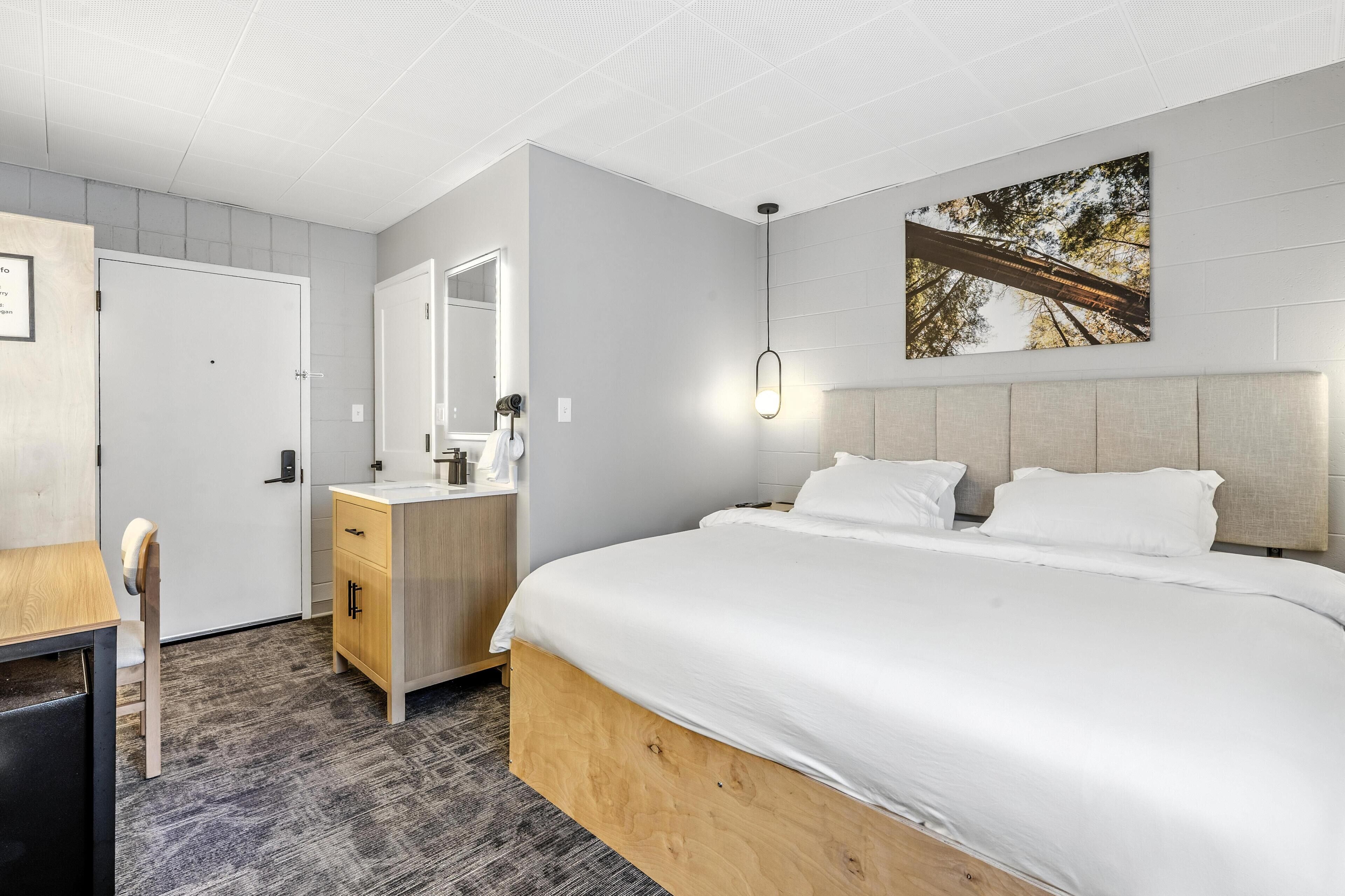 A modern hotel room with a large bed, a wooden dresser, a mirror, and a framed picture on the wall.