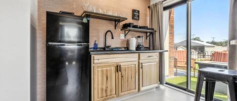 A modern kitchen with a black refrigerator, wooden cabinets, and a window overlooking a backyard.