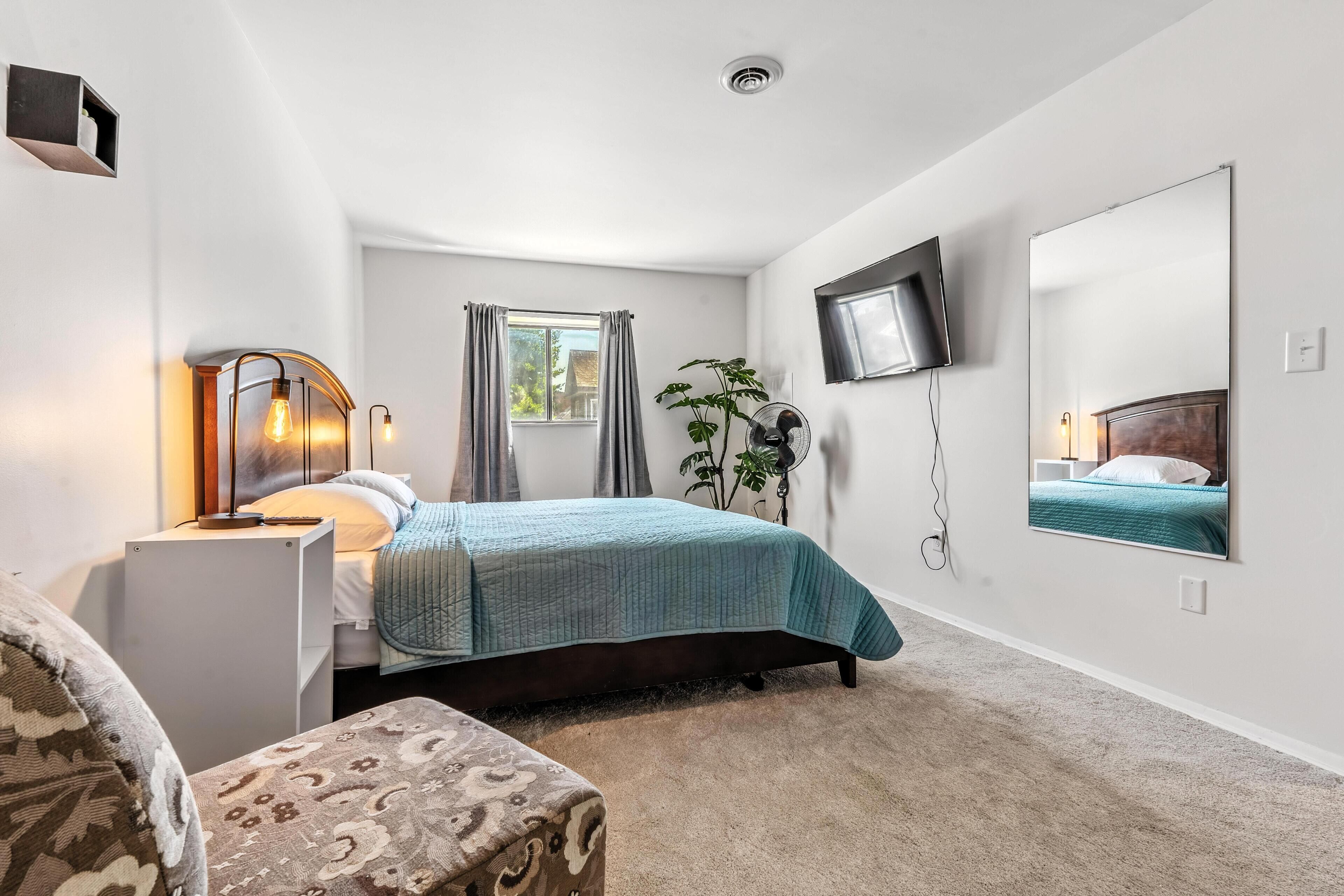 A bedroom with a bed, bedside table, lamp, TV, and a large mirror.