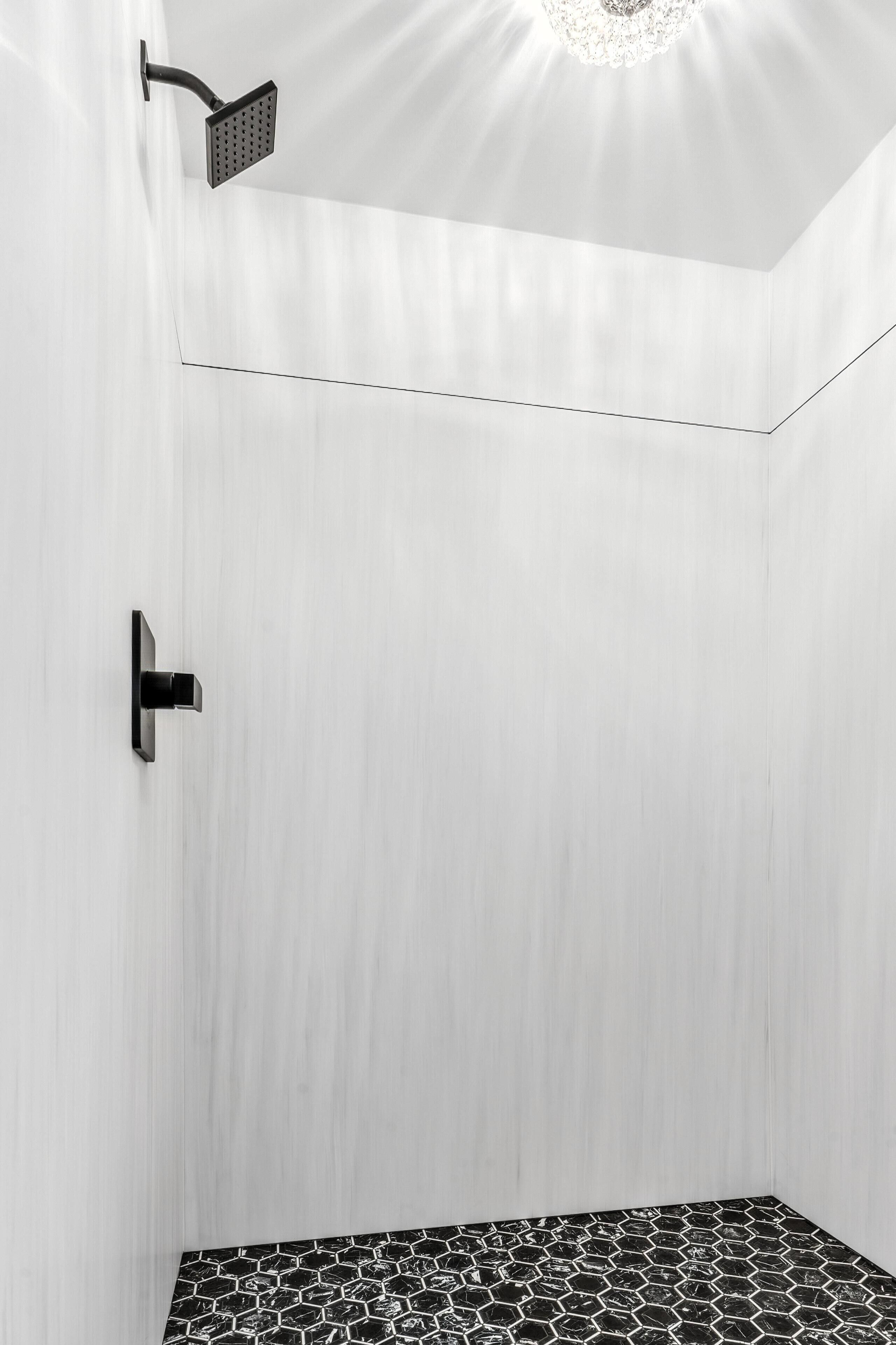 A modern shower with a black handle and a showerhead, a white textured wall, and a geometric black and white tile floor.