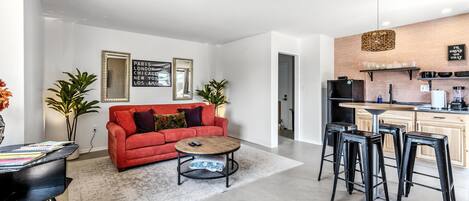 Een moderne woonkamer met een rode bank, een salontafel en een keuken met barstoelen.