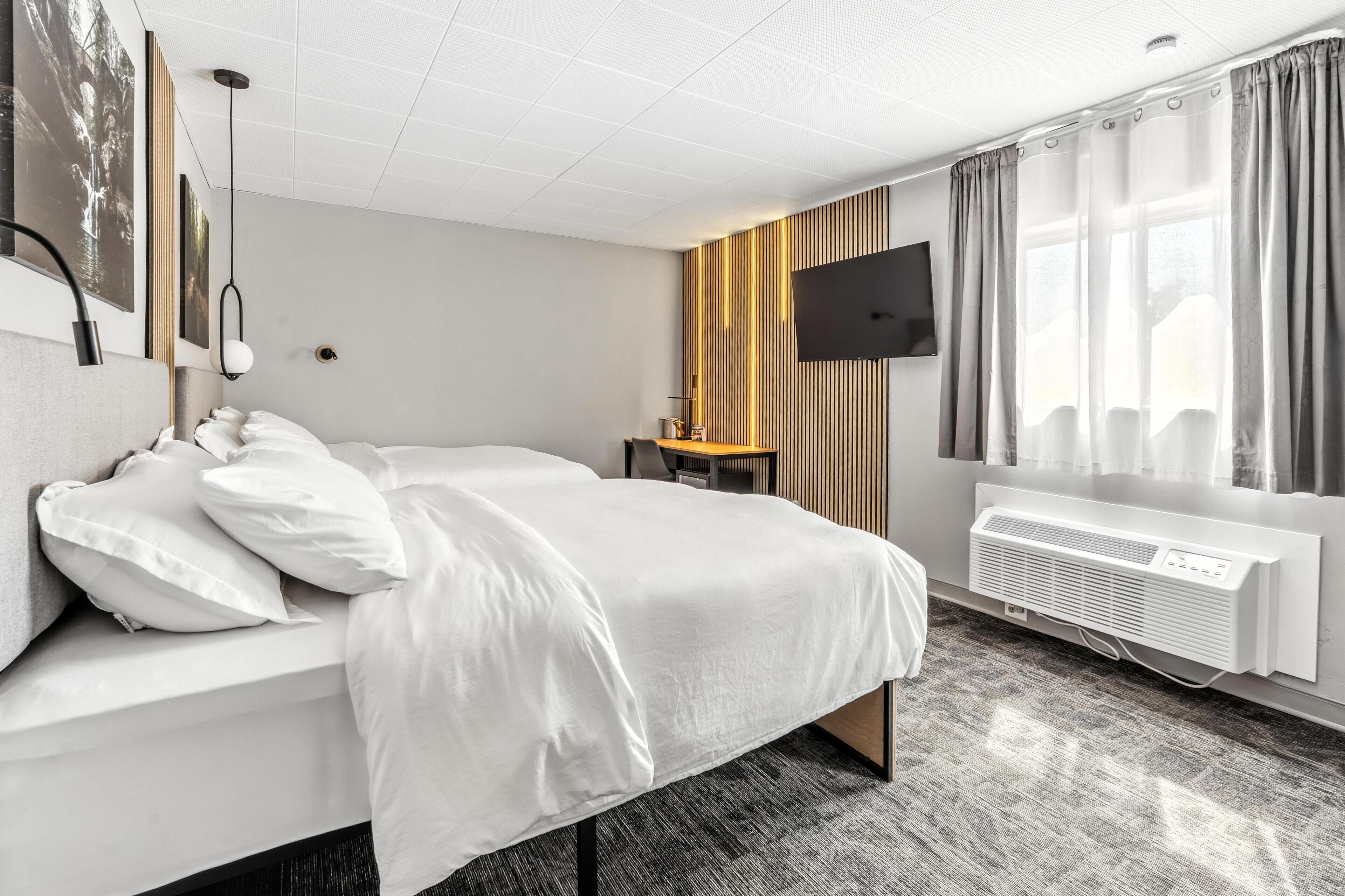 A modern hotel room with a large bed, a flat-screen TV, and a built-in air conditioning unit.