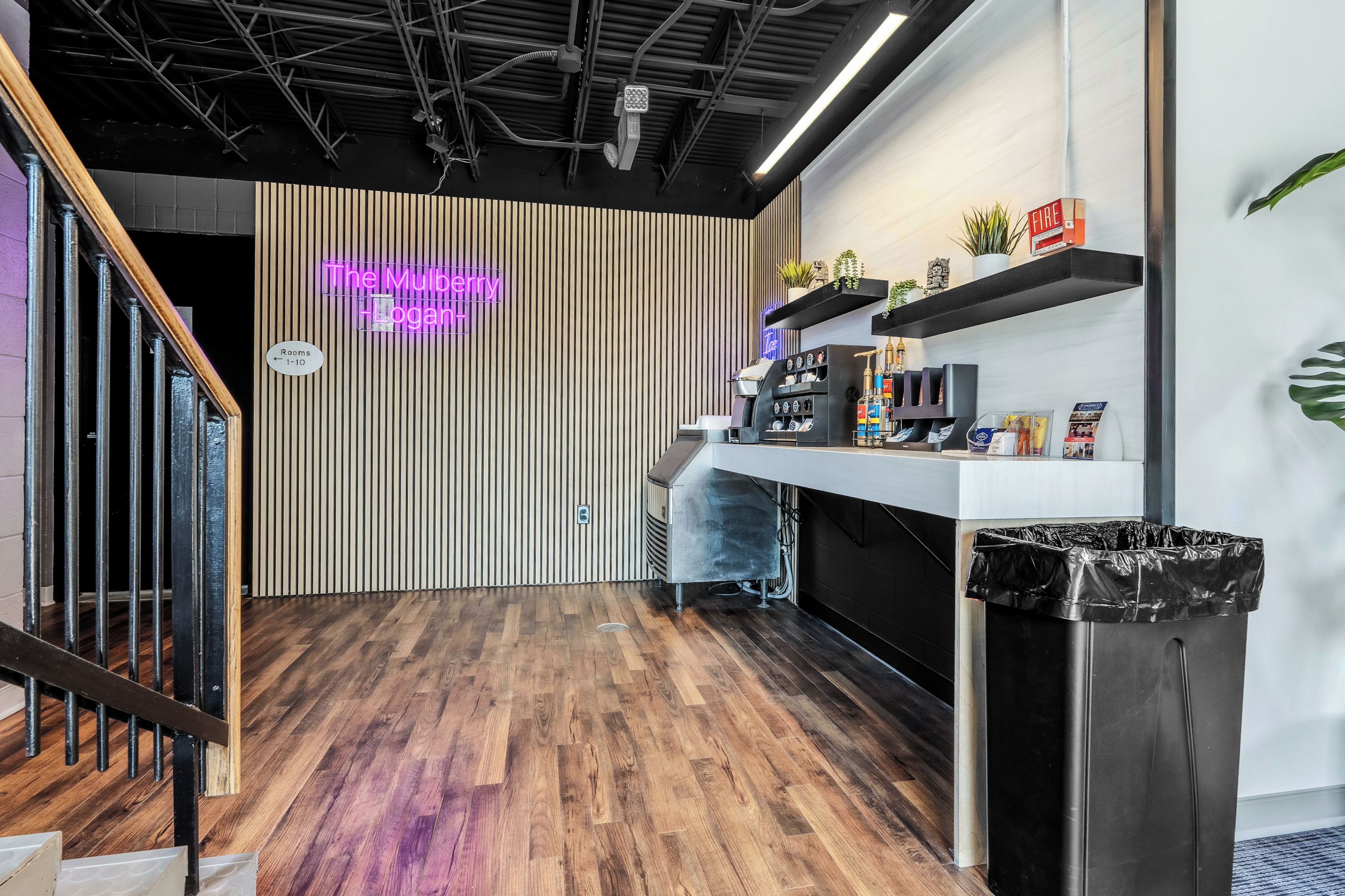 Een modern interieur met een houten vloer, een neonbord, een koffieapparaat en een prullenbak.