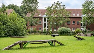 A grassy outdoor area with a wooden structure, trees, and a brick building with windows.