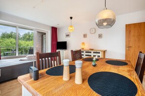 A dining area with a wooden table, black placemats, and a TV in the background.