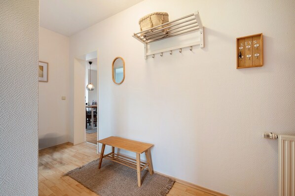 A room with a wooden bench, a hanging basket, a coat rack, a mirror, and a wall-mounted key holder.