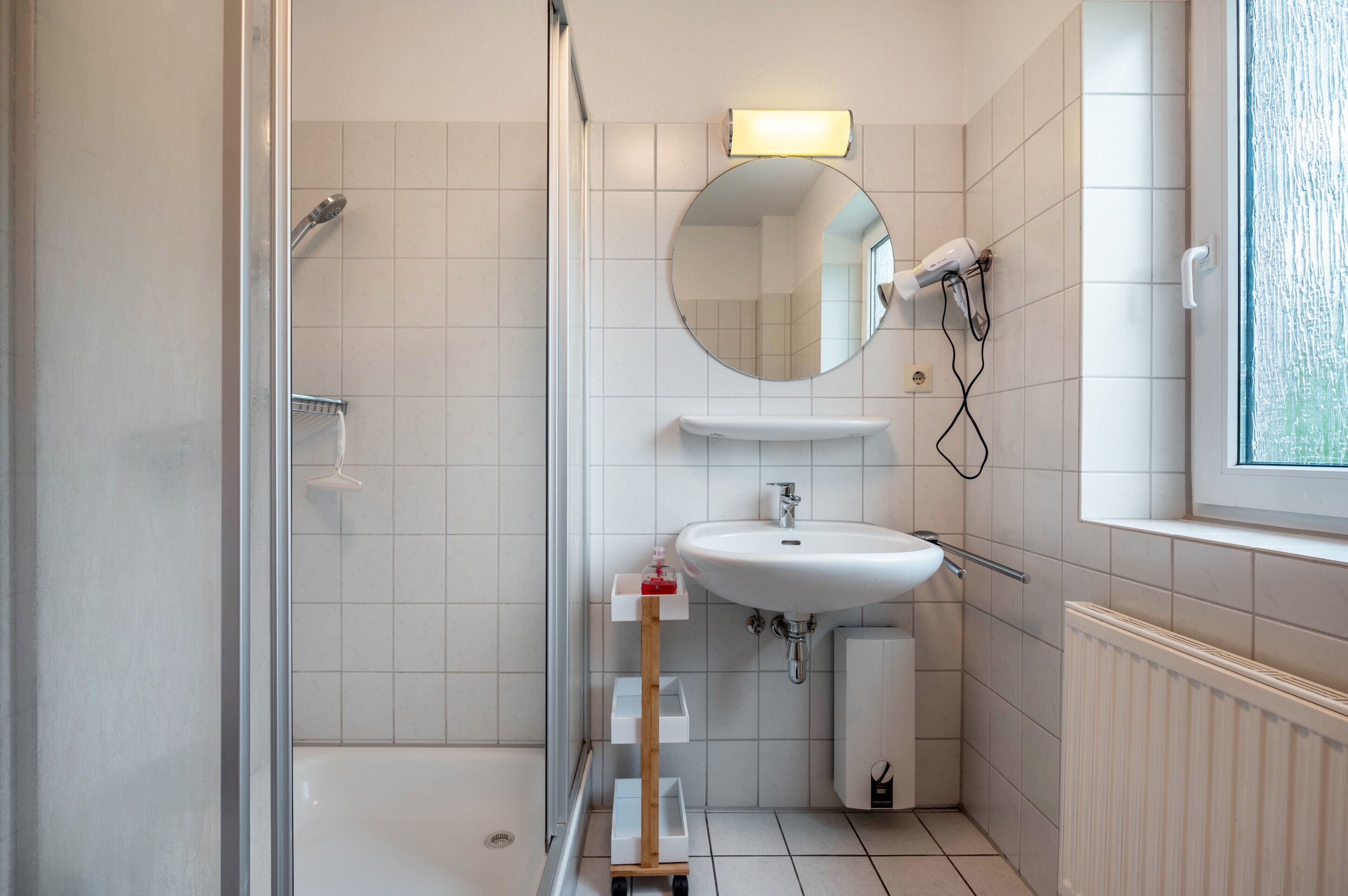 Un baño moderno con ducha, lavamanos, espejo y ventana.