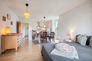 A modern room with a bed, bedside table, lamp, and a view of a kitchen and dining area.