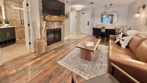 Una sala de estar con chimenea de piedra, un televisor de pantalla plana, un sofá de cuero y un comedor con mesa de madera.