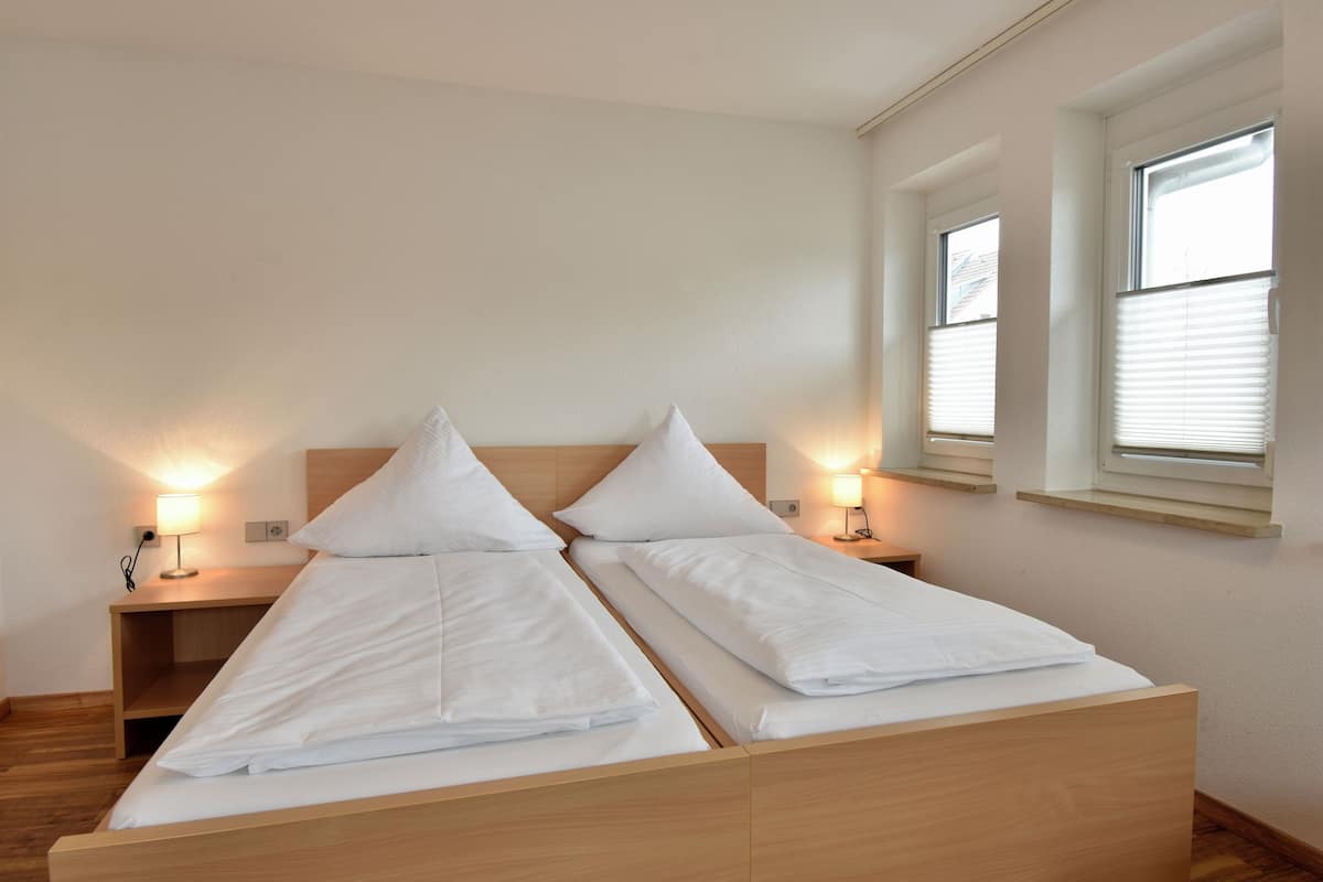 Habitación doble con dos camas, mesitas de noche, lámparas y ventanas.