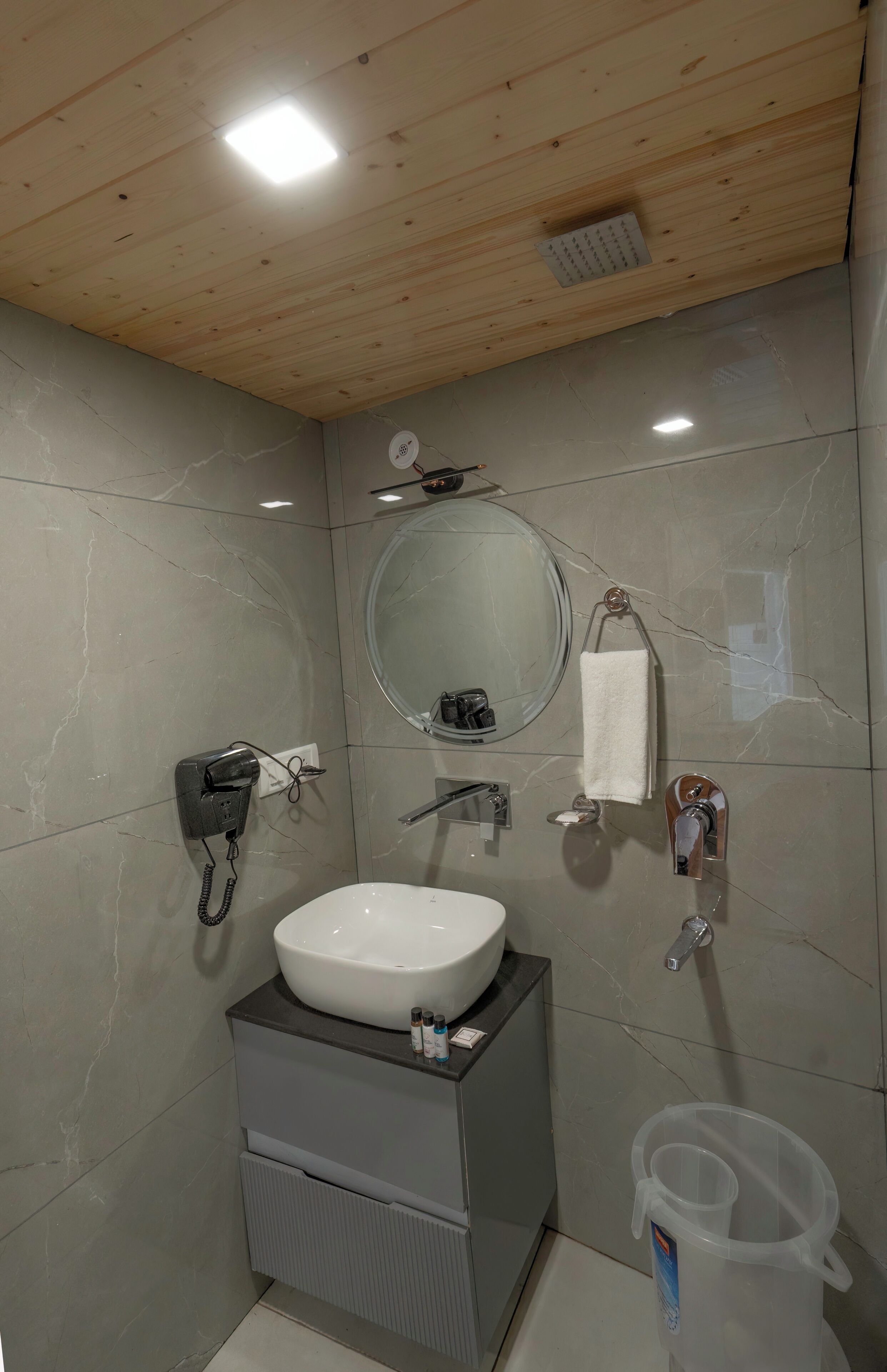 A modern bathroom with a wooden ceiling, a white sink, a mirror, a towel rack, and a handheld showerhead.