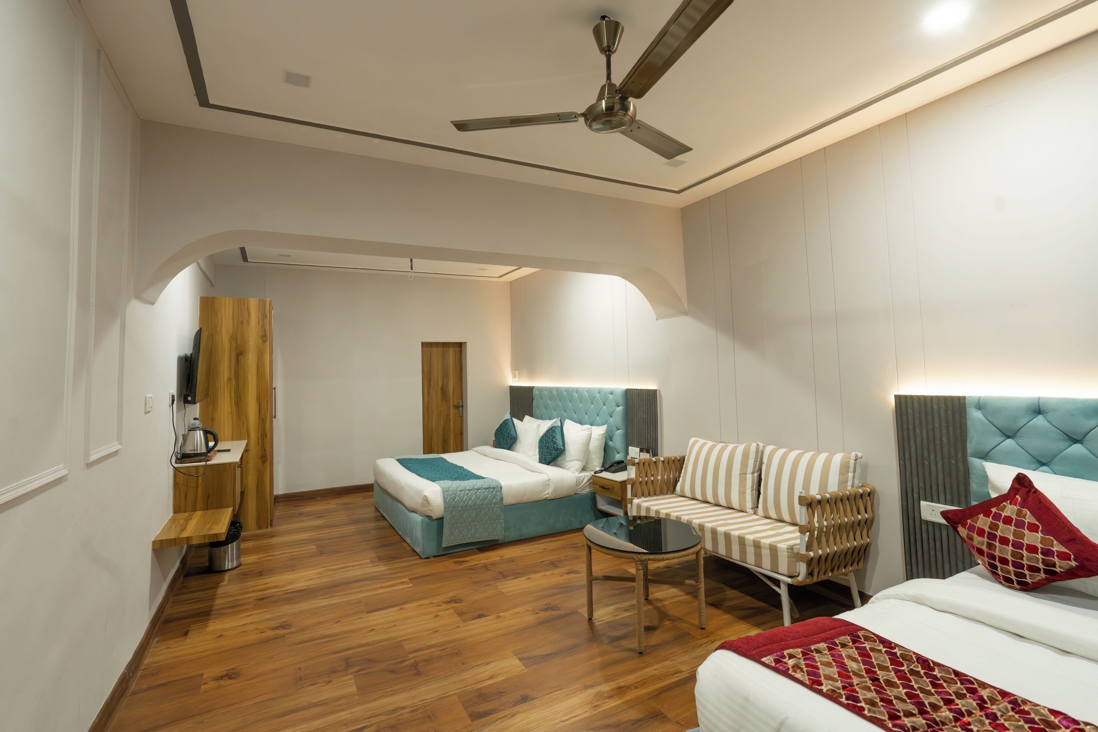 A modern hotel room with a bed, a sofa, a small table, a ceiling fan, and a wooden floor.