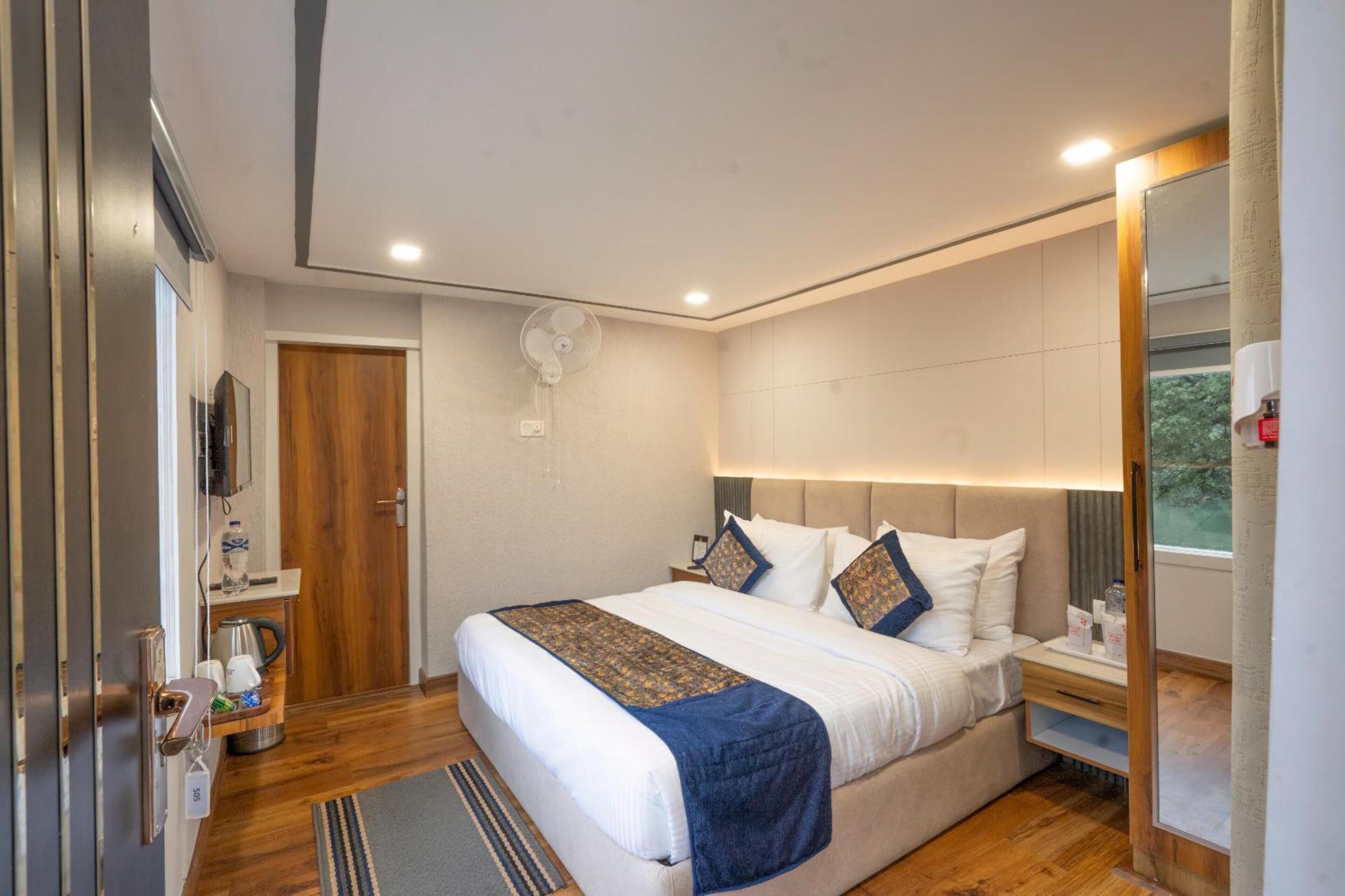 A modern hotel room with a large bed, bedside table, and a small desk.