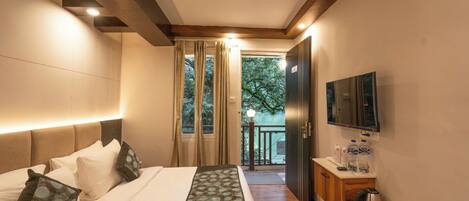 A modern hotel room with a large bed, a TV mounted on the wall, and a balcony with a view of trees.