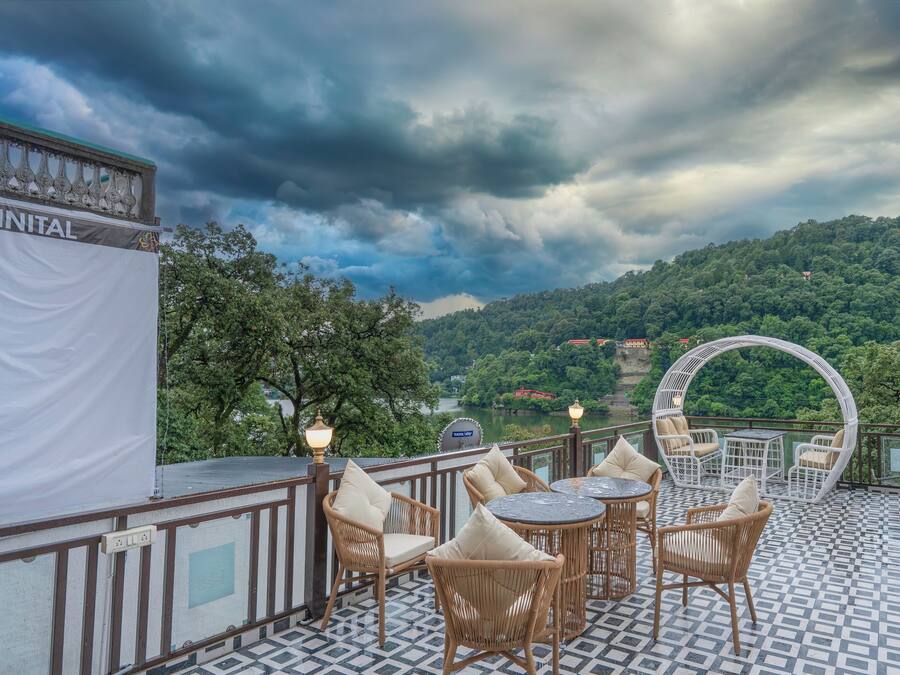 A terrace with wicker furniture, a view of a lake, and a sign reading 'NAINITAL'.
