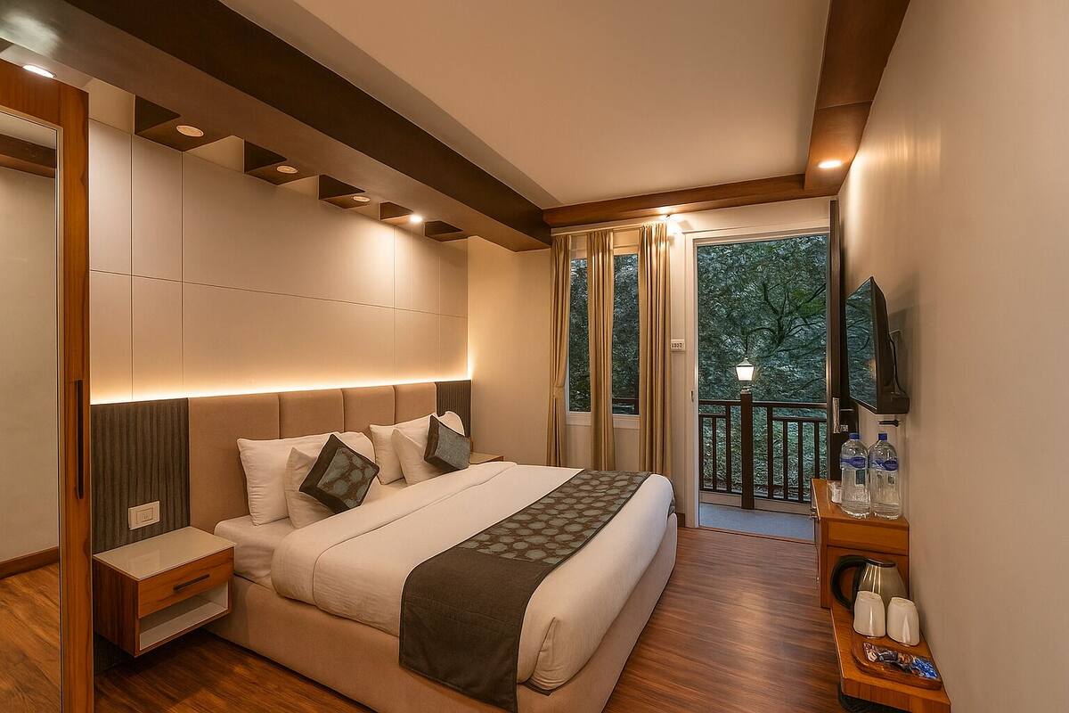 Ein modernes Hotelzimmer mit einem großen Bett, einem Nachttisch, einem kleinen Tisch, einem Balkon mit Blick auf Bäume und einem Fernseher.
