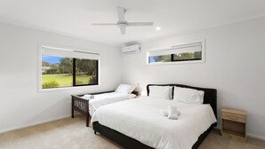 A bedroom with a large bed, two bedside tables, a ceiling fan, and a window with a view of a garden. - Beach Road Bliss in Rhyll (Rhyll)