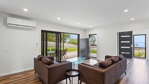 A modern living room with a glass table, two sofas, and a large sliding glass door leading to a backyard. - Beach Road Bliss in Rhyll (Rhyll)