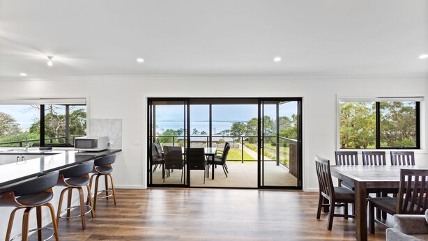 A modern kitchen with a large island, bar stools, and a dining area with a view of the sea. - Beach Road Bliss in Rhyll (Rhyll)