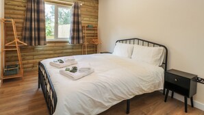 Ein ordentlich bezogenes Bett mit weißen Leinentüchern und Handtüchern, ein Holzboden, ein schwarzes Metall-Kopfstück, ein kleiner Nachttisch und ein Fenster mit Vorhängen.