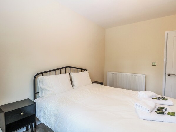 Un lit simple avec une literie blanche, une tête de lit en métal noir, une petite table de chevet et un radiateur blanc.