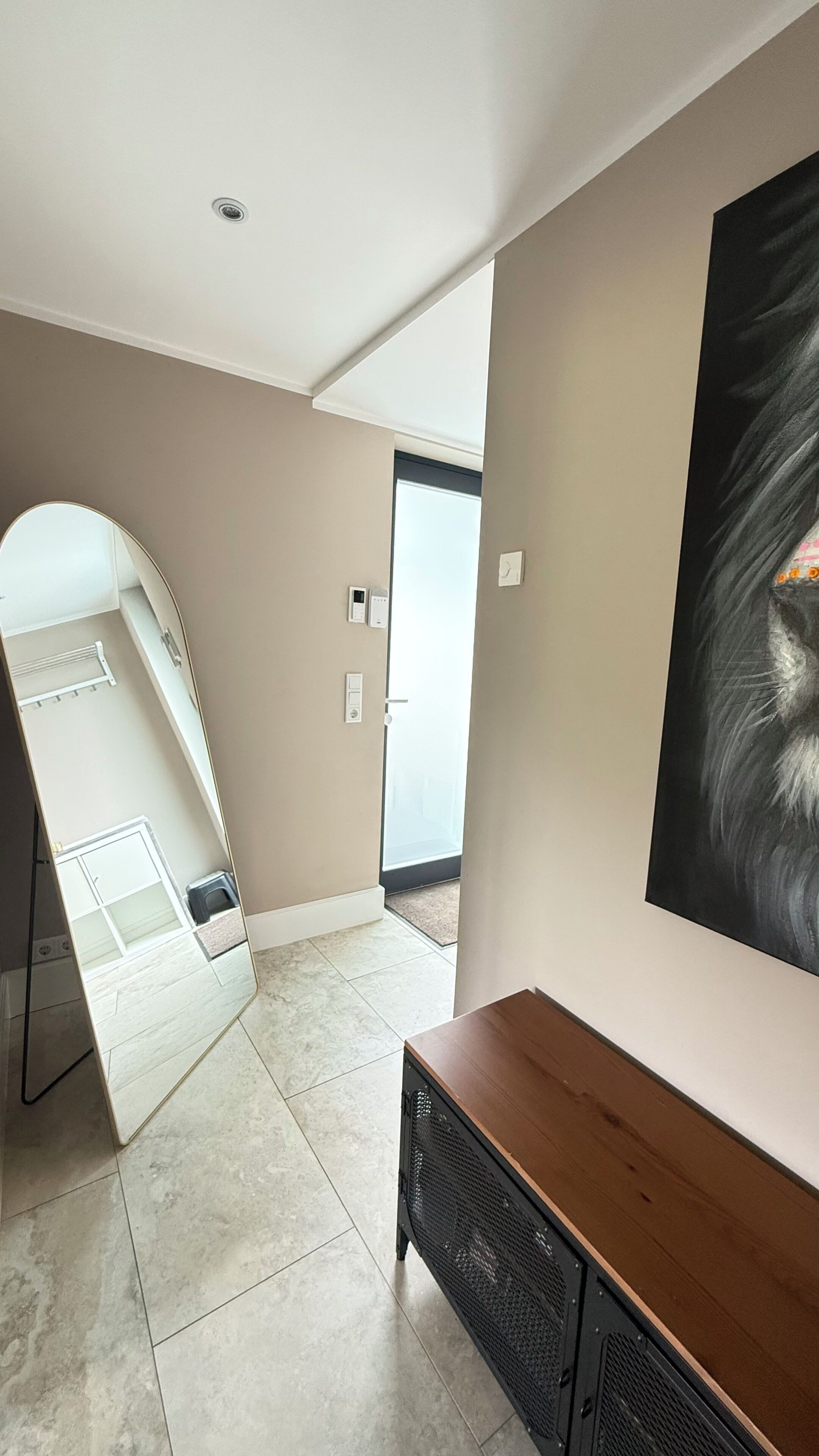 Un interior moderno con un espejo grande, una consola de madera y un cuadro en la pared.