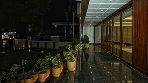 A modern hotel exterior with a glass facade, a well-lit entrance, and potted plants lining the walkway. - Hotel Malsi Mist (Dehradun)