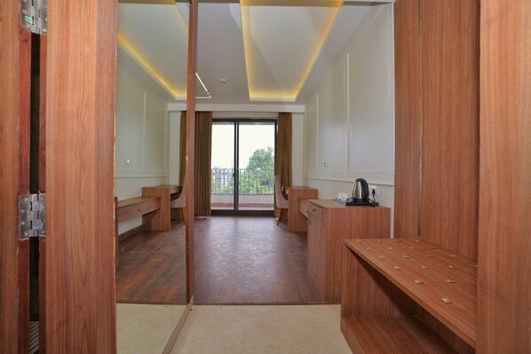 Habitación de hotel con suelo de madera, un escritorio con hervidor y vistas al exterior a través de un ventanal.