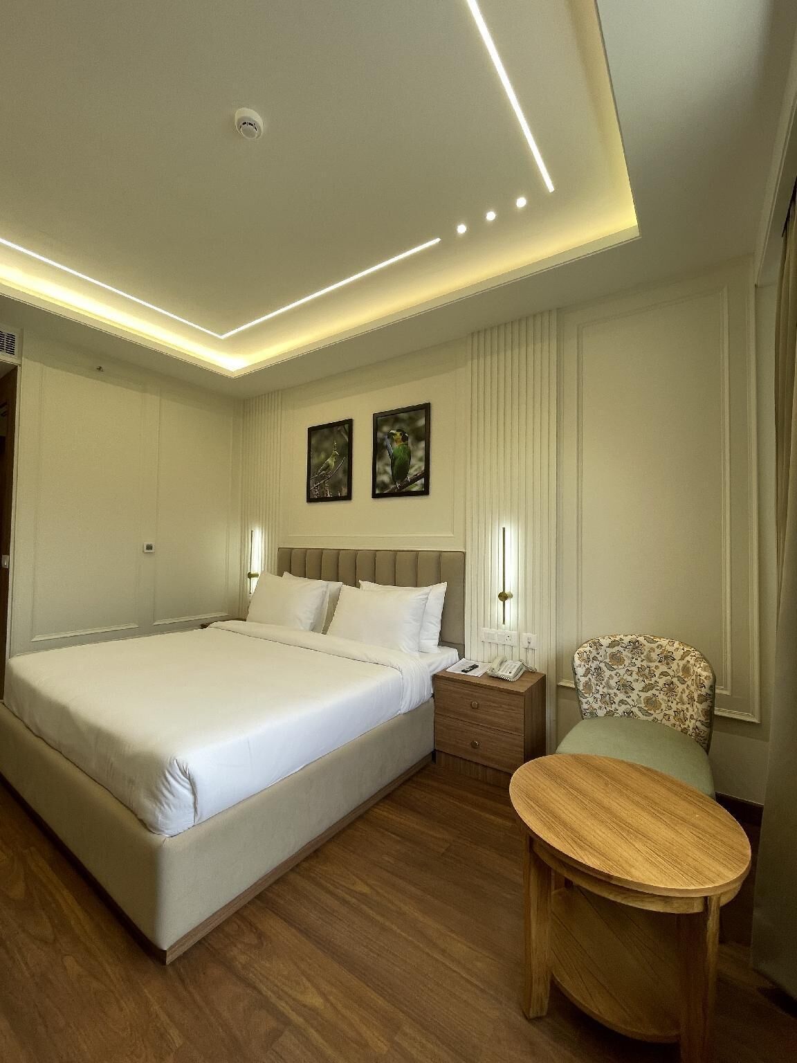 A modern hotel room with a large bed, bedside tables, a small round table, and two framed pictures on the wall.