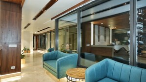 A modern lobby with blue sofas, a round wooden table, and large glass windows. - Hotel Malsi Mist (Dehradun)