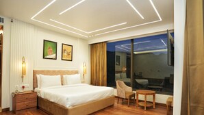 A modern hotel room with a large bed, bedside tables, a seating area, and a large window offering a view. - Hotel Malsi Mist (Dehradun)