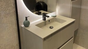 A modern bathroom with a large mirror, a sink, and a black soap dispenser.