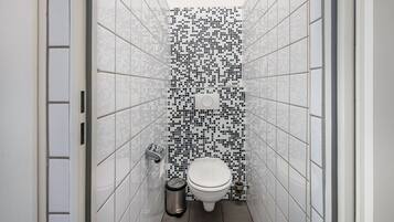 A narrow bathroom with a tiled wall, a toilet, a trash bin, and a hand dryer.