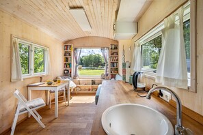 A compact kitchen with a sink, a dining area with a table and chairs, and a view of the outdoors through a large window. - Tiny Home 'Mit Blick Auf Den See' with Private Garden, Wi-Fi and Air Conditioning (Fitzen)