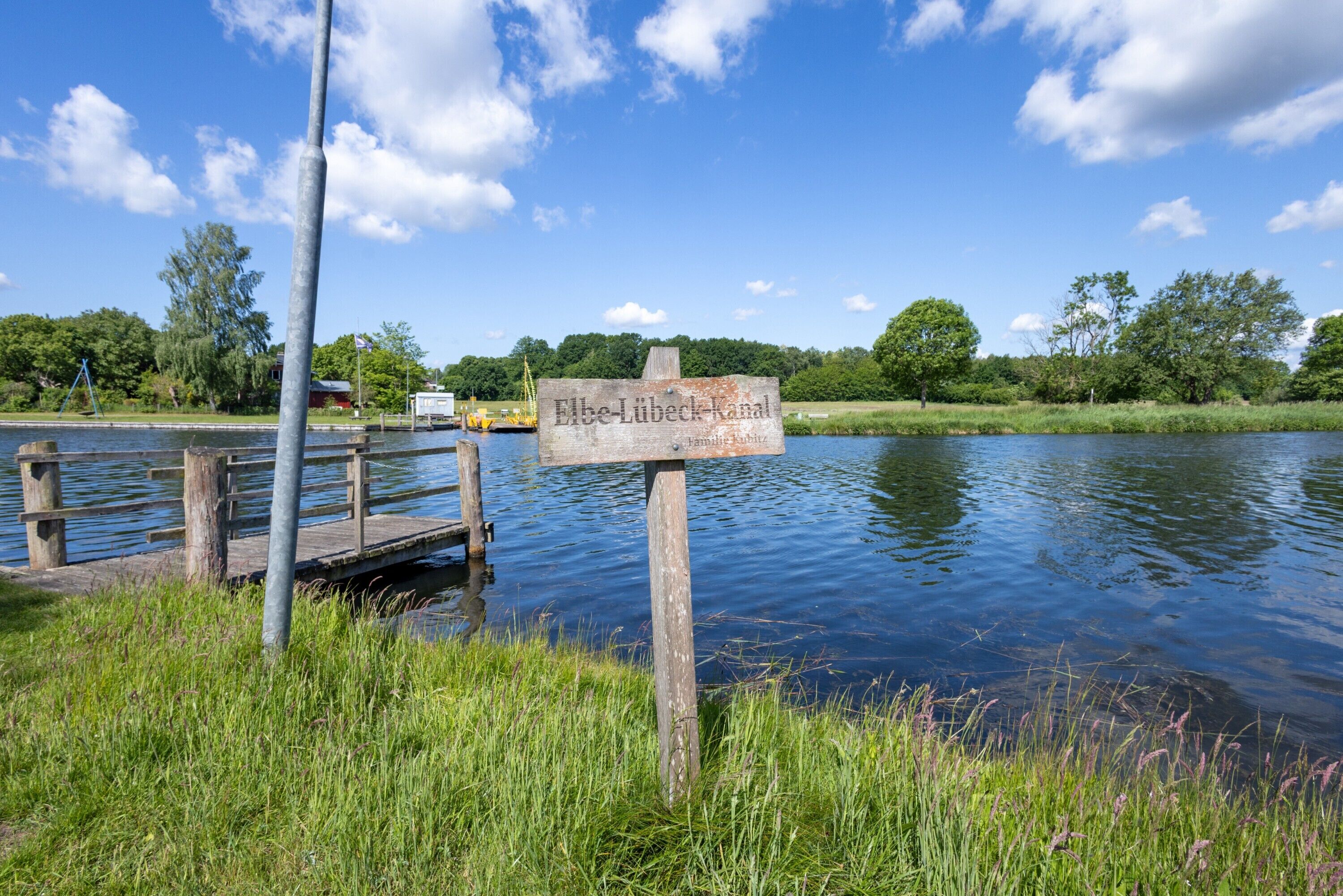 Un panneau indicateur en bois, près d’un lac paisible, sous un ciel dégagé.