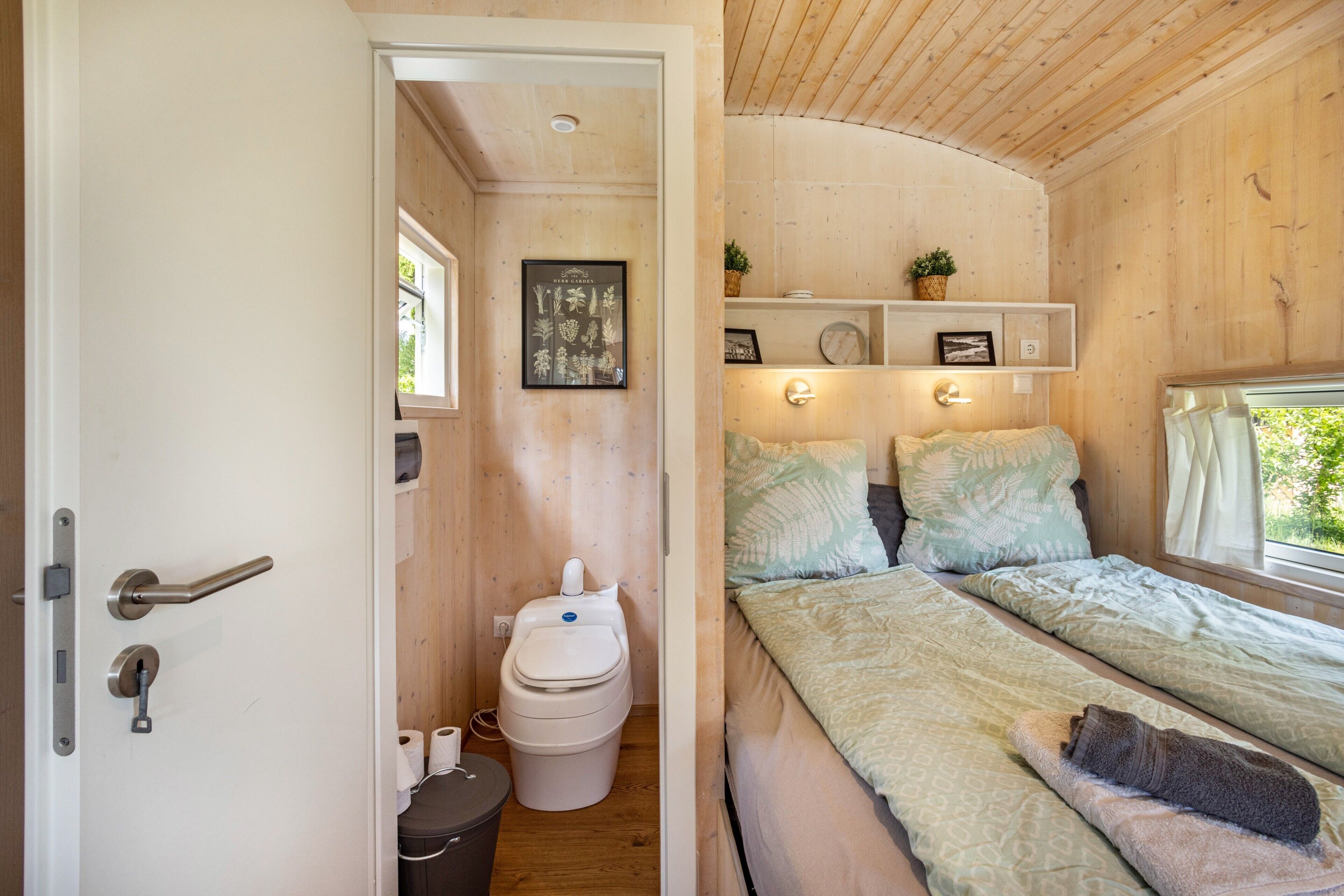 A wooden interior with a bed, a toilet, and a shelf with decorative items.
