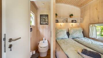 A wooden interior with a bed, a toilet, and a shelf with decorative items.