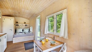Een gezellig chaletinterieur met een houten plafond, een bed met kussens, een eettafel met stoelen en een raam met gordijnen.