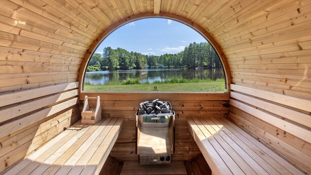 Een sauna met een houten interieur, een bankje en uitzicht op een meer en bos.