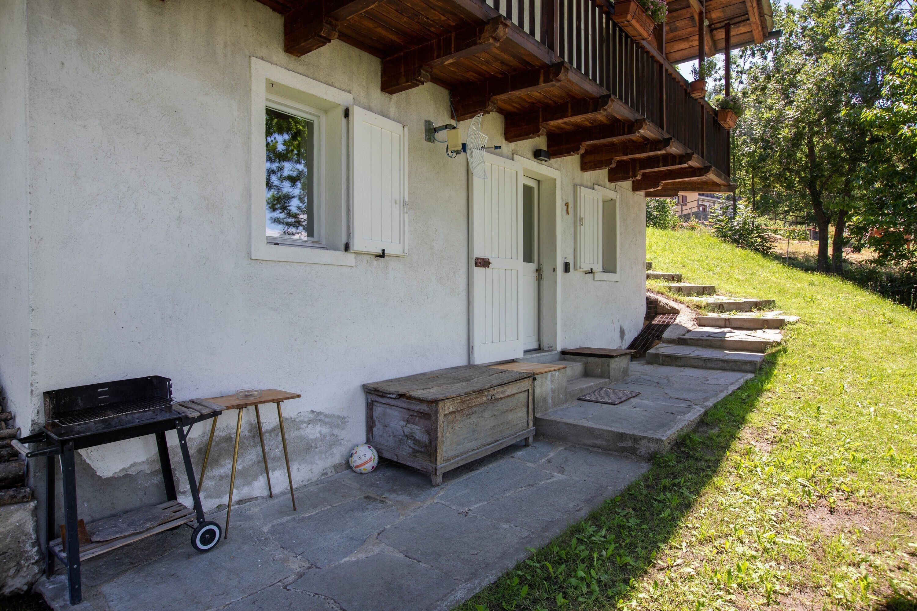 Un edificio de fachada blanca, con escalones de madera, una parrilla y una pequeña mesa.