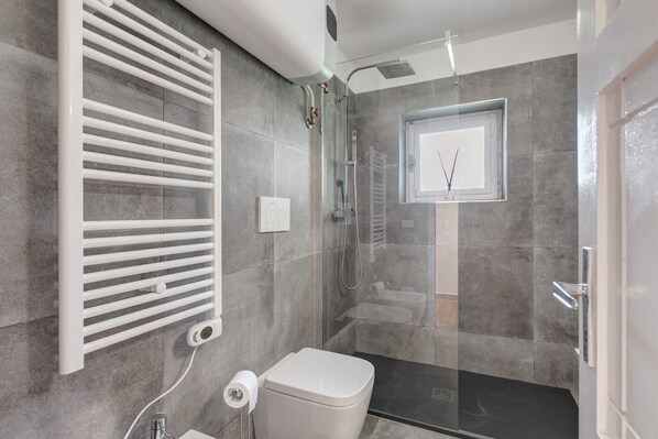 Une salle de bain moderne avec une douche à parois de verre, des toilettes blanches et un porte-serviettes.