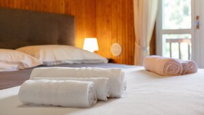 Een net opgemaakt bed met opgerolde handdoeken, een houten hoofdbord en een lampje op het nachtkastje.