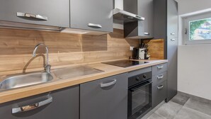 Een moderne keuken met grijze kastjes, een houten aanrechtblad, een roestvrijstalen spoelbak en een inbouwoven.