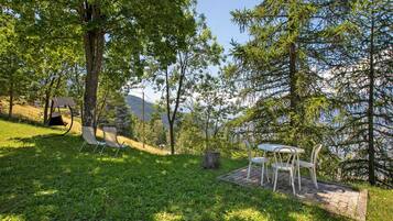 Un espace extérieur verdoyant avec une table et des chaises, un banc en bois et un arbre.