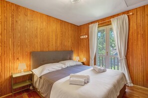 A wooden-paneled room with a bed, nightstand, and curtains.