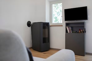 Une pièce dotée d’un radiateur moderne de couleur sombre, d’un téléviseur à écran plat fixé au-dessus d’une bibliothèque, et d’une fenêtre donnant sur des arbres.