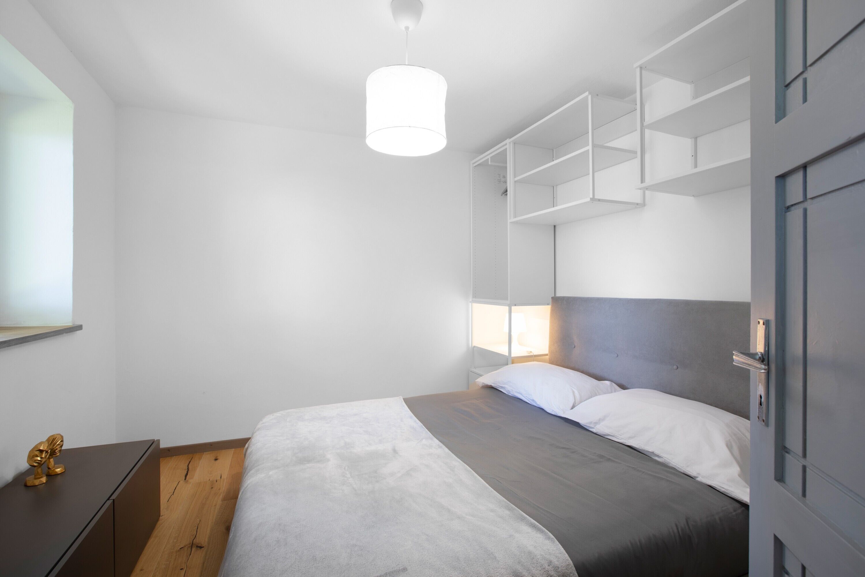 Un dormitorio moderno con cama, estanterías empotradas y una lámpara colgante.