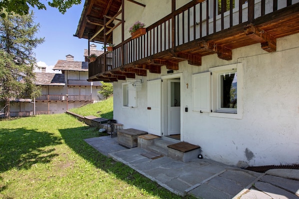 A traditional chalet with a wooden balcony, stone steps, and a small outdoor seating area.