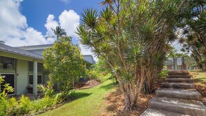 A residential property with a well-maintained lawn, a concrete staircase, and a variety of tropical plants.